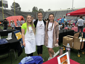 three people pose at the Culinary Medicine booth on the field at War Memorial Stadium