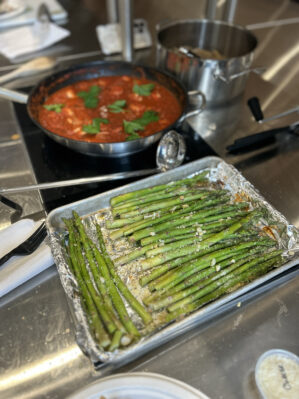 close up of asparagus on a tray with a skillet of sauce in the background