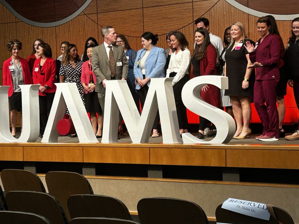 UAMS Faculty and staff standing with the Chancellor behind large UAMS letters