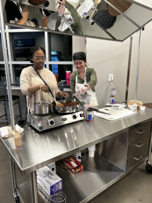 two women cooking on a display cooking table with a mirror on top