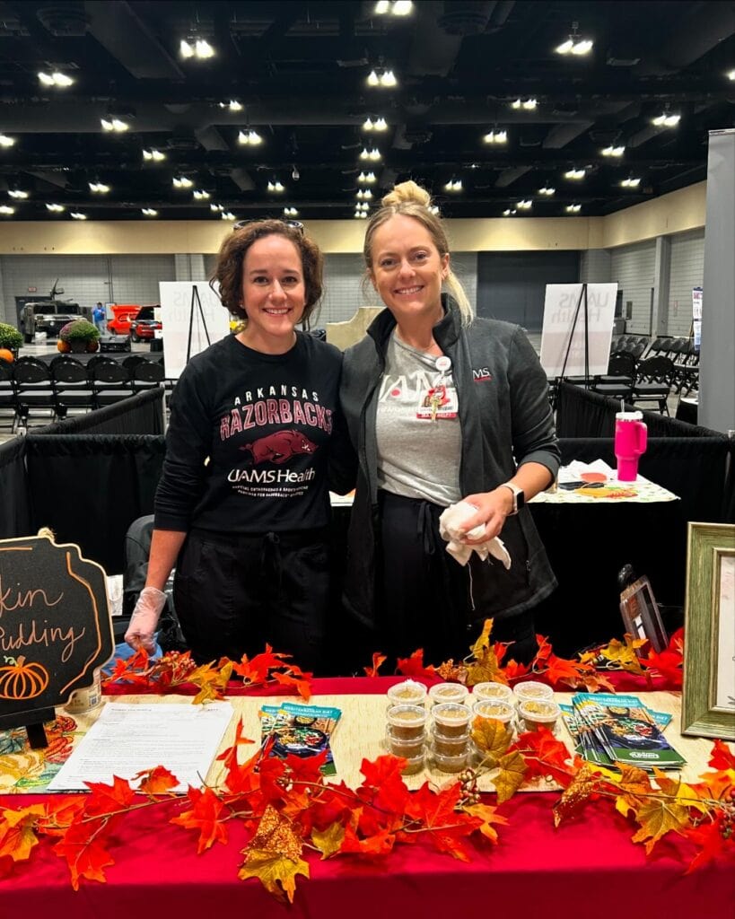 two women standing at a table in a convention center. The table is decorated for Fall