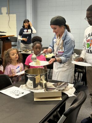 A faculty member serves food to a line of children