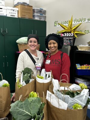 Two women pose by grocery sacks full of fresh greens