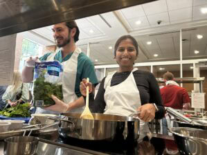 Two students cooking together in the teaching kitchen. They are both standing by the stove. 